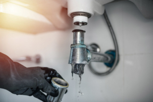 A person wearing black gloves holds a metal faucet tightly in their hand.