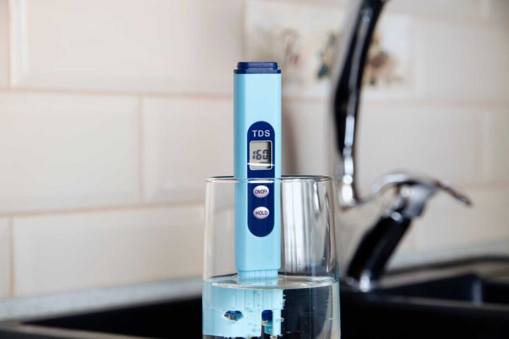 A digital thermometer submerged in a glass of water, displaying the current temperature.