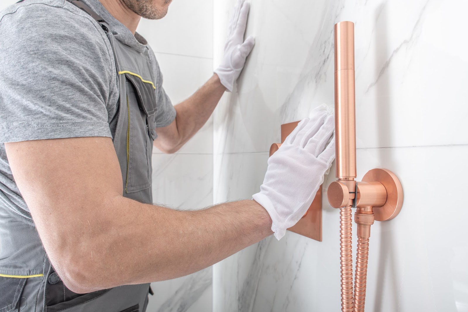 A contractor in white shirt and gloves fixing a shower head in a bathroom remodel project