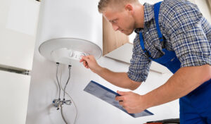 A Man In Overalls Inspecting A Tankless Water Heater For Installation Or Replacement By A Water Heater Specialist