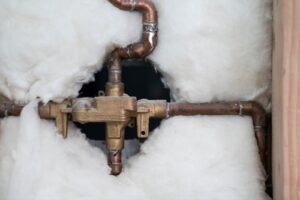 Copper pipes and brass valve partially encased in white insulation within a wooden frame.