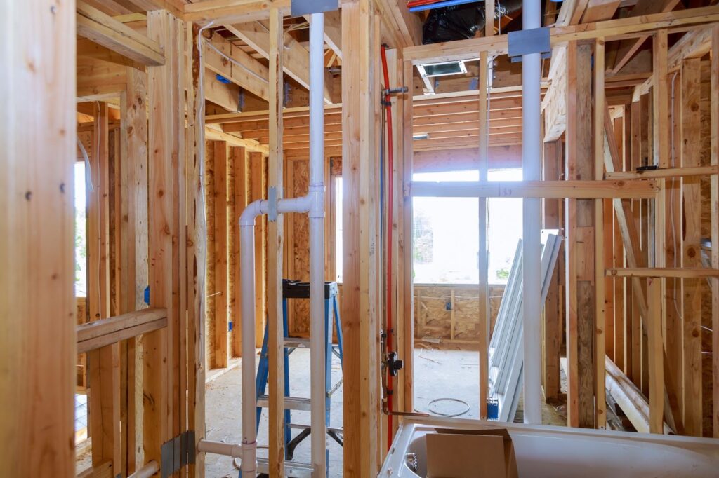 Wooden framework of a building under construction with plumbing pipes and a ladder.