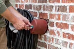 A man uses a hose to wash a brick wall, addressing stains from recent plumbing pipe repairs.