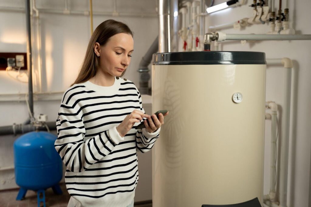 A woman stands in front of a water heater focused on her cell phone while checking information or making a call