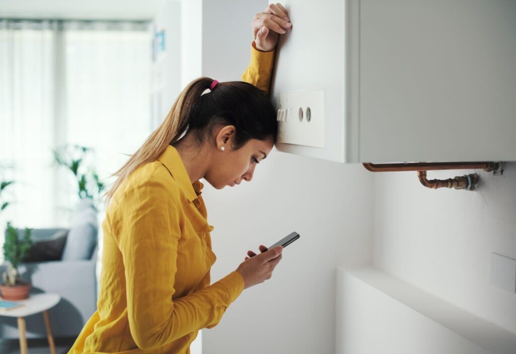woman stands in front of a wall focused on her phone with a thoughtful expression on her face