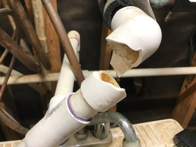 A broken white pipe in a bathroom with water leaking onto the floor indicating a plumbing issue